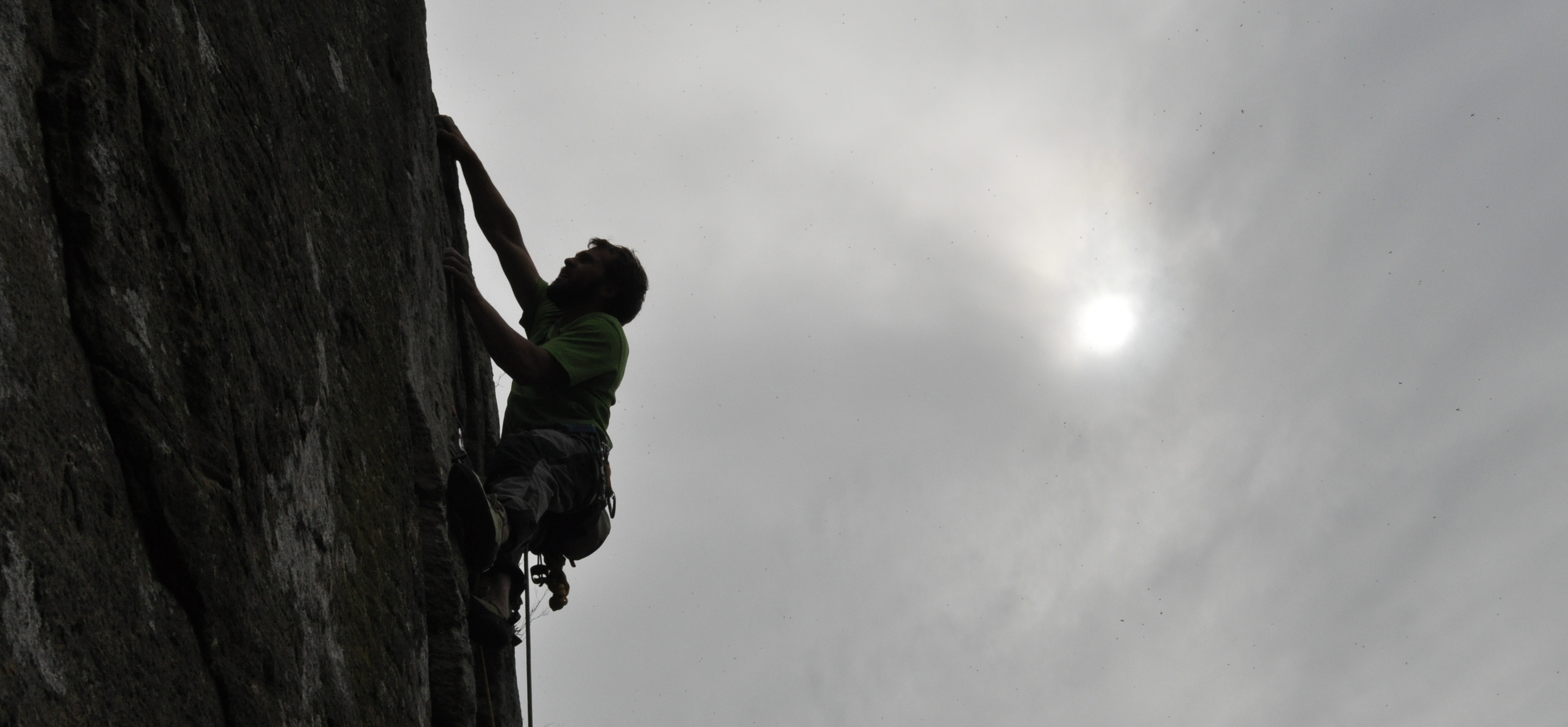 Climber silhouetted against a pale sky on a steep rock face