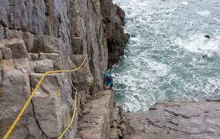 Climber on a sea cliff above crashing waves in Pembroke