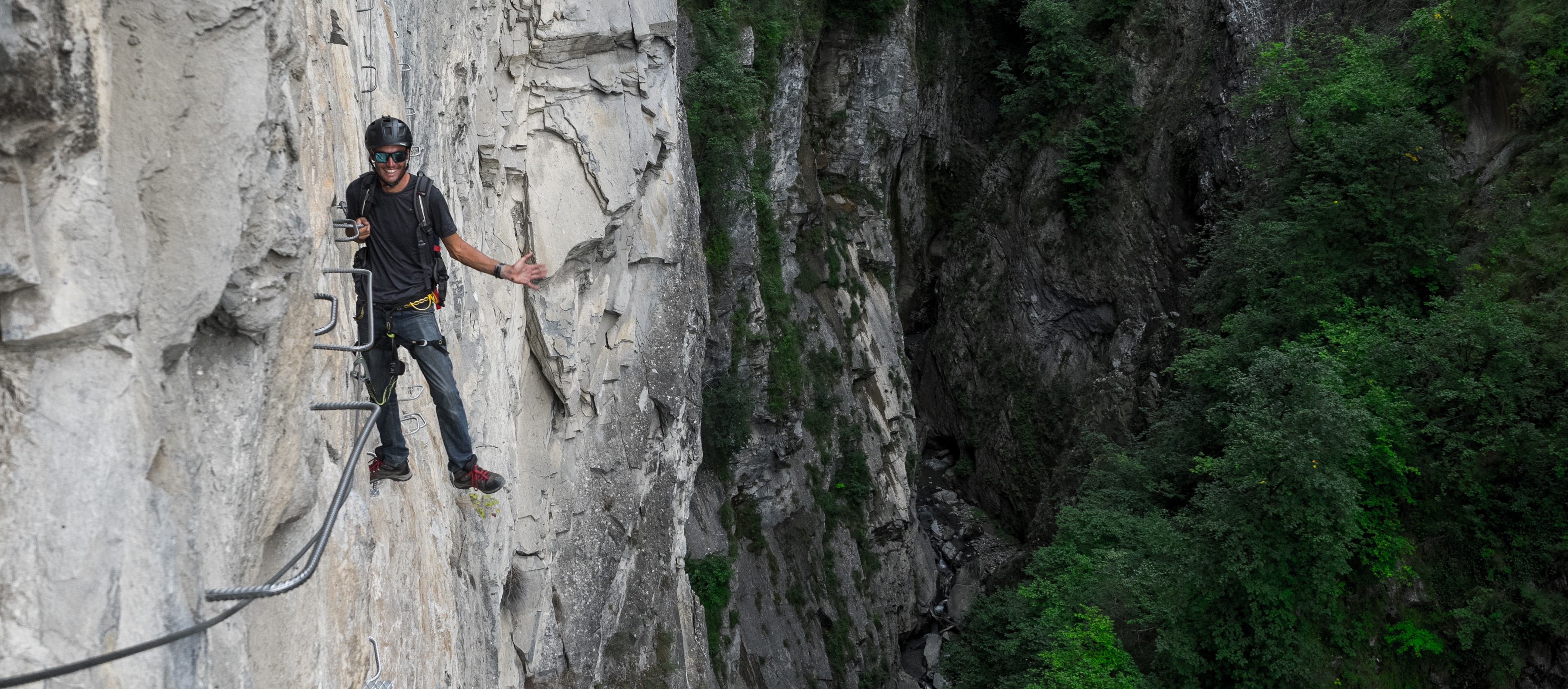 Climber on a via ferrata cable up a tall limestone face