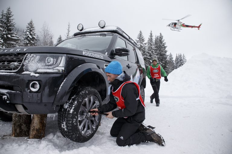 Driver kneeling by a Land Rover in deep snow on a car event in the Alps