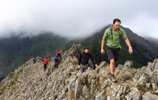 Welsh 3000s Challenge walkers scrambling up a rocky ridge in low cloud
