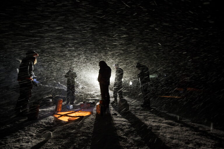 Film crew silhouetted by headtorches in heavy snow at night