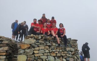 Lake District summit shelter Team in red sitting on a dry-stone summit shelter in the Lake District