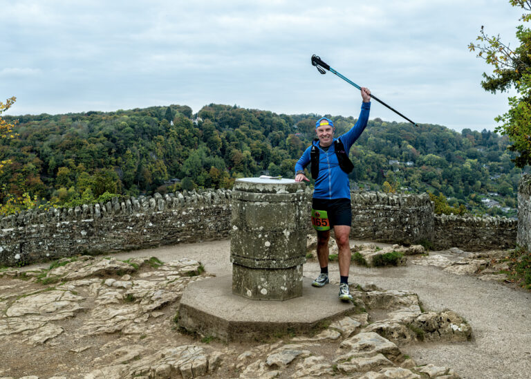 Runner celebrating at the Symonds Yat Rock trig point with the Wye Valley behind