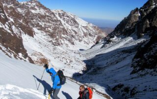 Walkers climbing a snowy slope towards Toubkal in the High Atlas