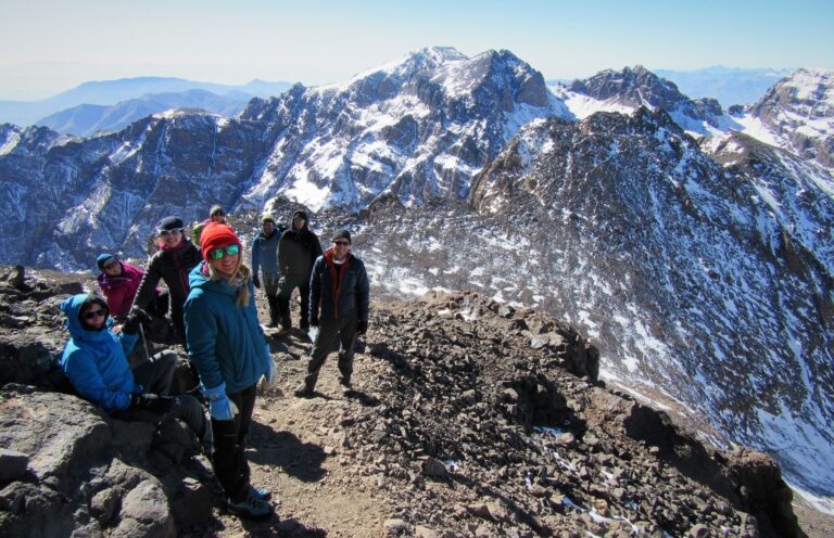 Trekkers on a rocky ridge below the snowy peaks of Toubkal in Morocco