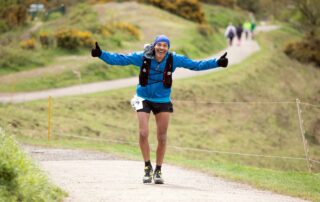 Runner with arms outstretched on a grassy trail on the Malvern Hills