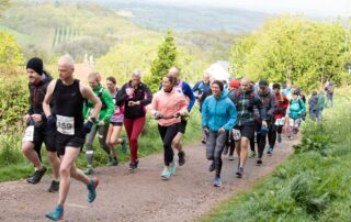 Pack of runners climbing a wide grassy trail on the Malvern Hills