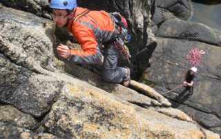Climber in an orange jacket pulling up a granite crack on a learn to lead course