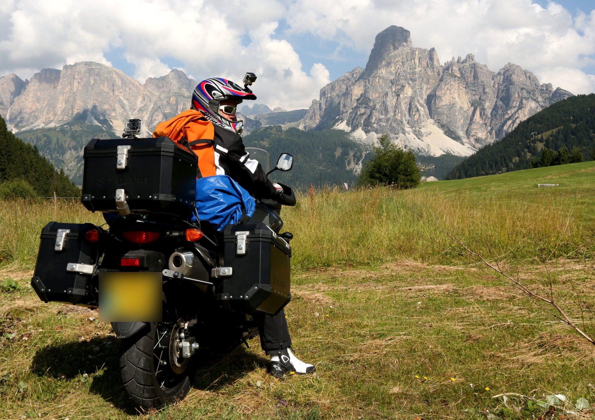 Dave Talbot on a loaded adventure motorbike in an Alpine meadow below the jagged limestone peaks of the Dolomites