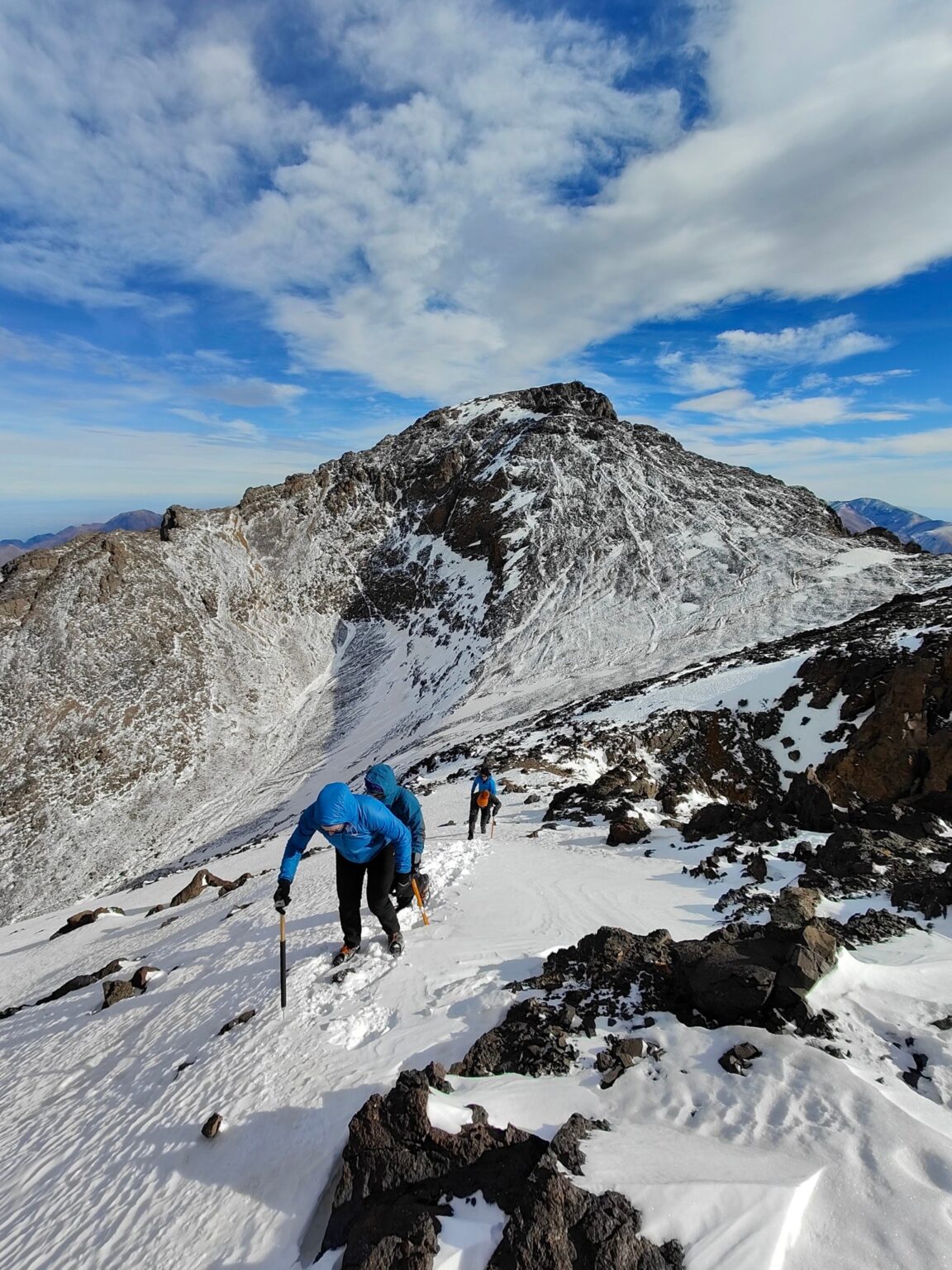 Climber ascending a snowy ridge with an ice axe