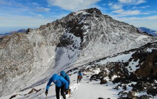 Climber ascending a snowy ridge with an ice axe