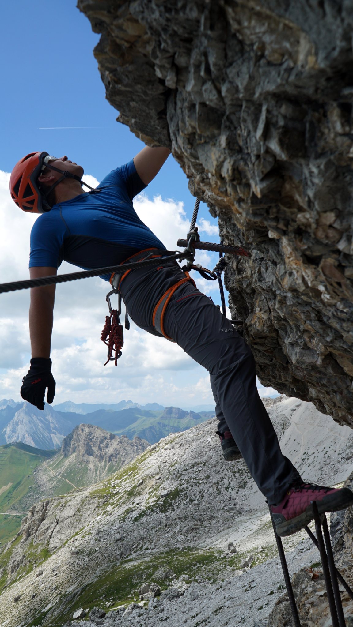 Climber clipped to a via ferrata cable high above alpine peaks